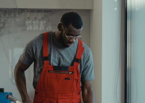 Man wearing red overalls using a mop indoors, depicting cleanliness and manual work.